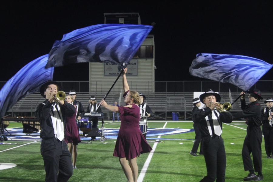The color guard swings their flags in the air while the band plays their music.