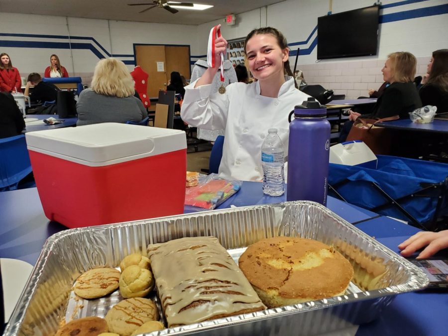 Junior Chase Nagel shows off her gold medal as she stands next to her baked creampuffs, caramel toffee cookies, pumpkin pecan loaves and a cake
