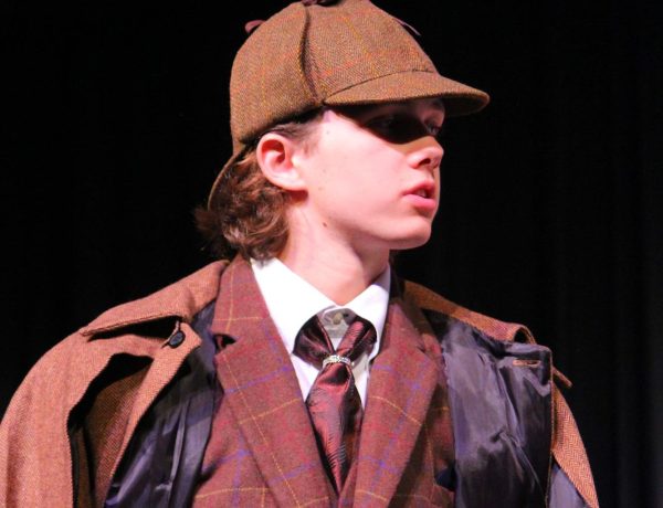 Sherlock Holmes(Chase Schnaible) stands in the middle of the stage. 