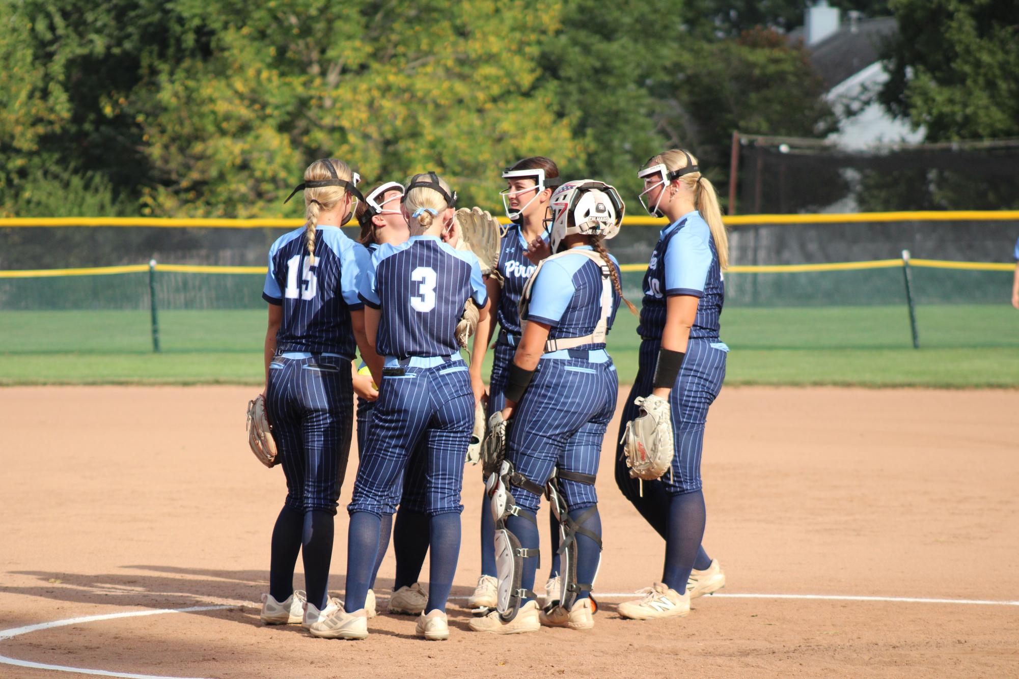 The softball team huddles on the mound in between batters.