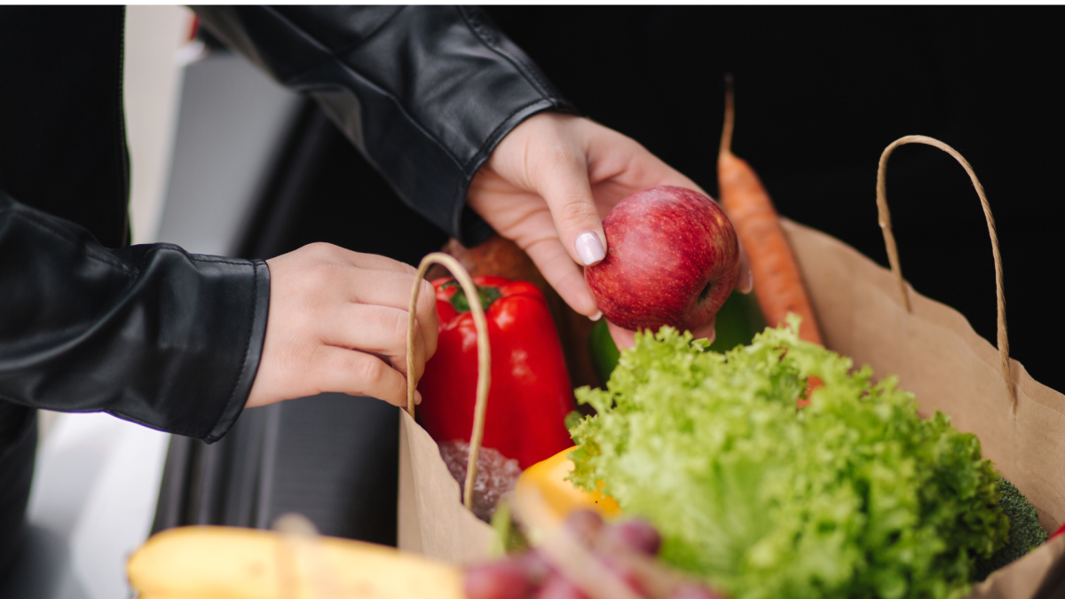 A person taking groceries out of a paper bag.
