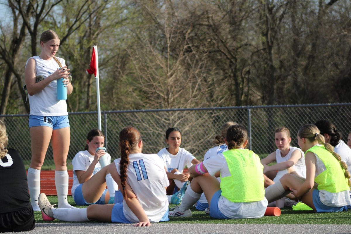 Varsity girls soccer team sitting down on the sidelines while playing against Lutheran High School.